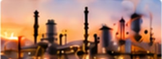 A refinery at dusk with towers and pipework lit by an orange sky.